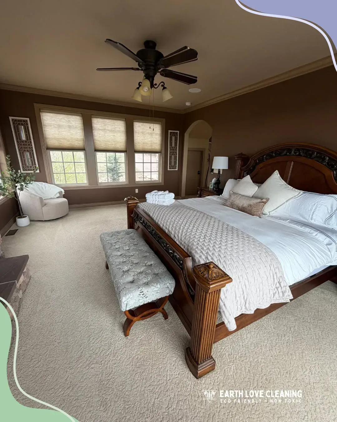 Spacious bedroom with large bed, bench, chaise lounge, and windows under a ceiling fan.