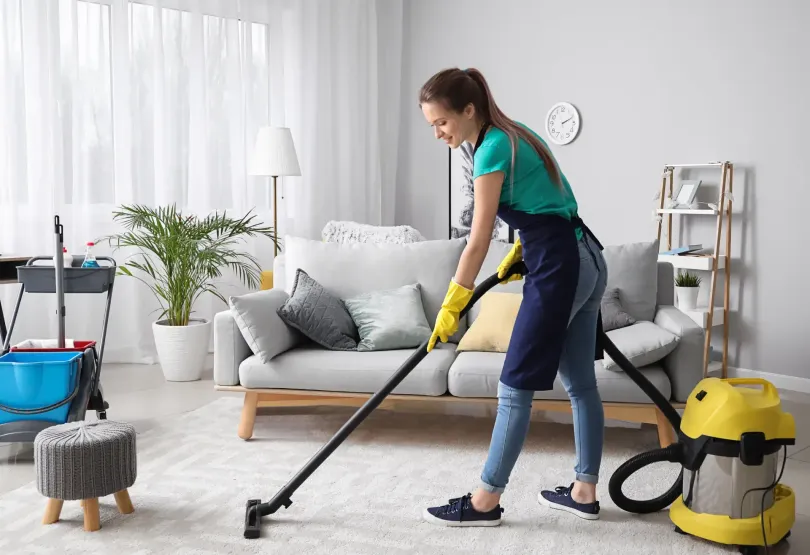 Professional cleaner vacuuming carpet in a clean residential living room.
