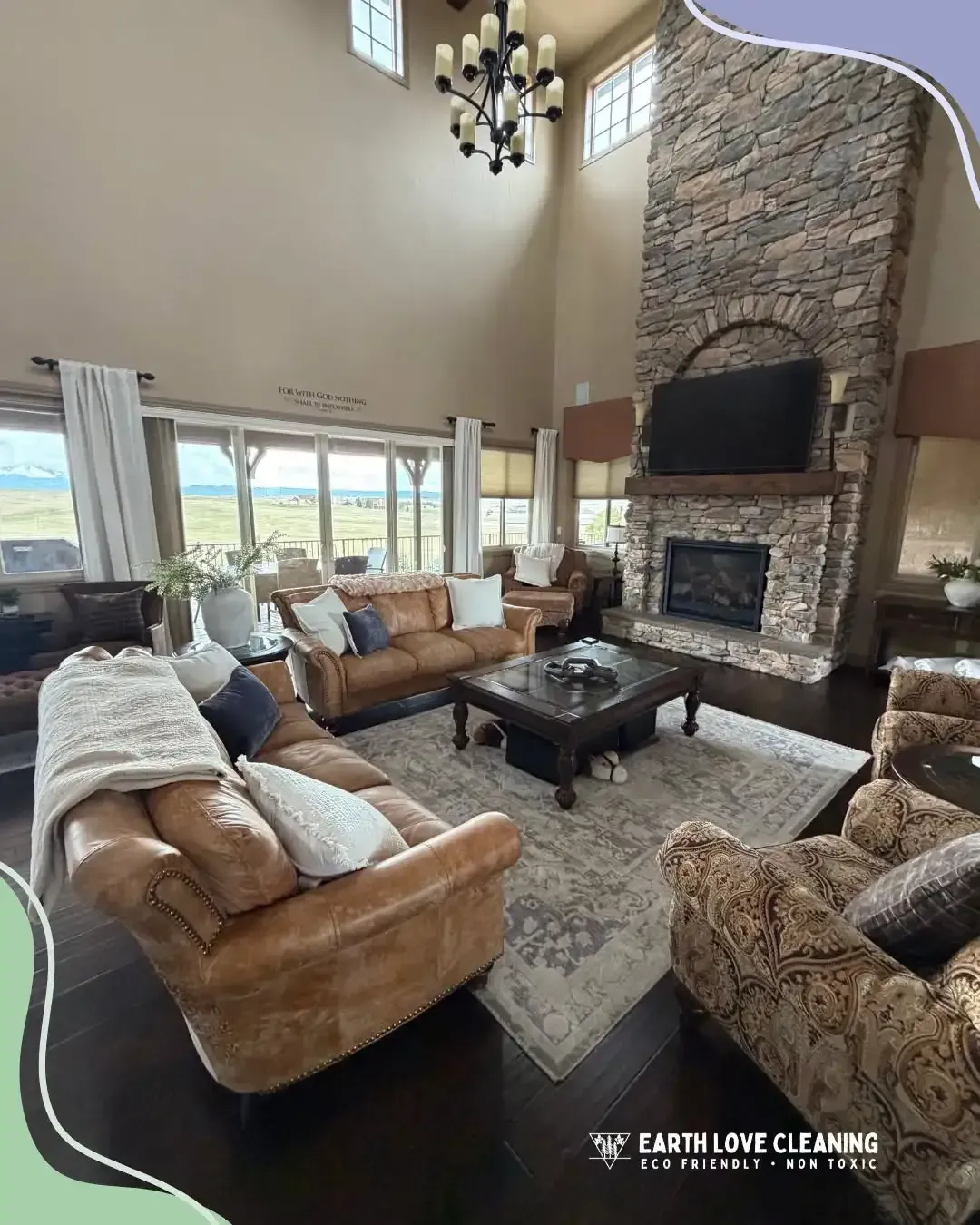 Living room with tall stone fireplace, tan sofas, large windows, and chandelier