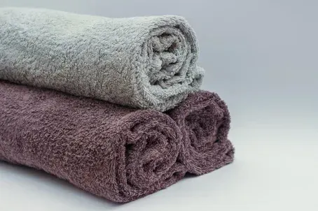 Two rolled towels, one light gray and one mauve, stacked on a white surface