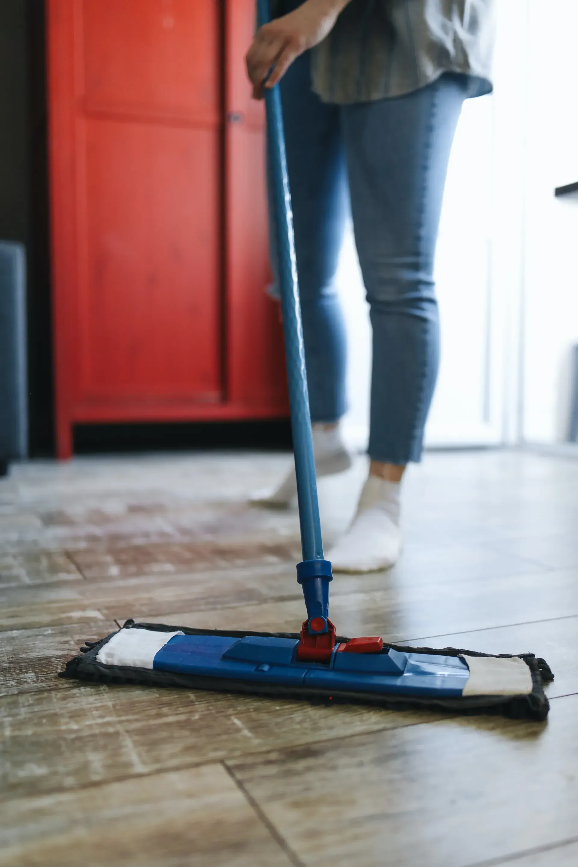 Person mopping a tiled floor with a blue mop in a bright room
