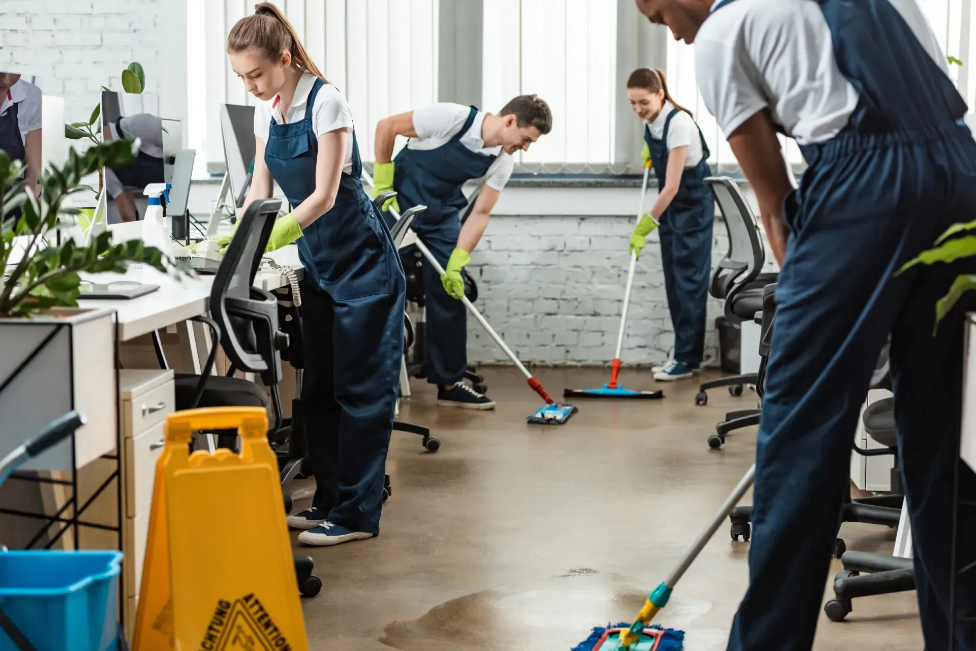 Janitors cleaning an office floor with mops and supplies beside desks and plants