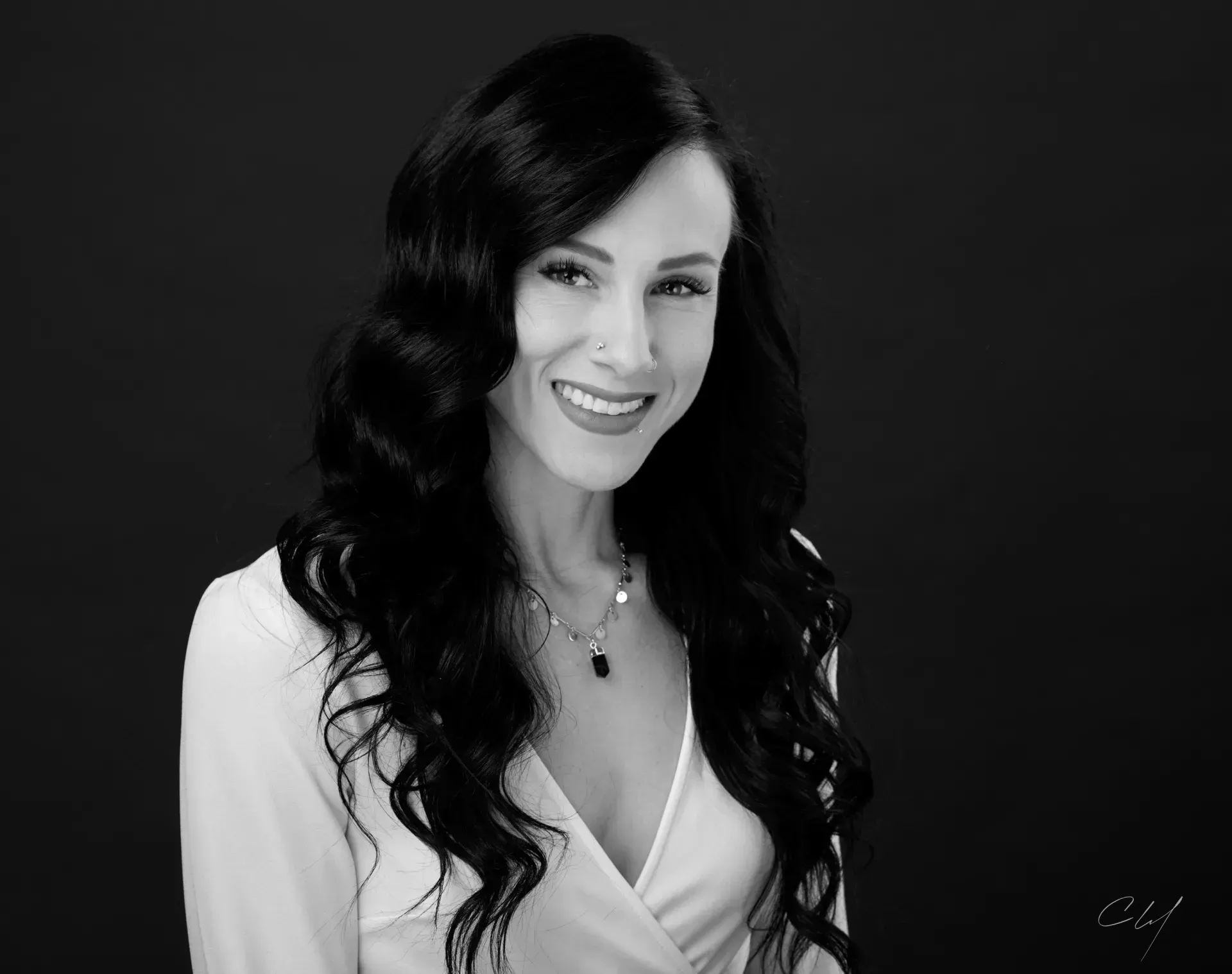 Smiling woman with long dark hair in a white top against a dark background