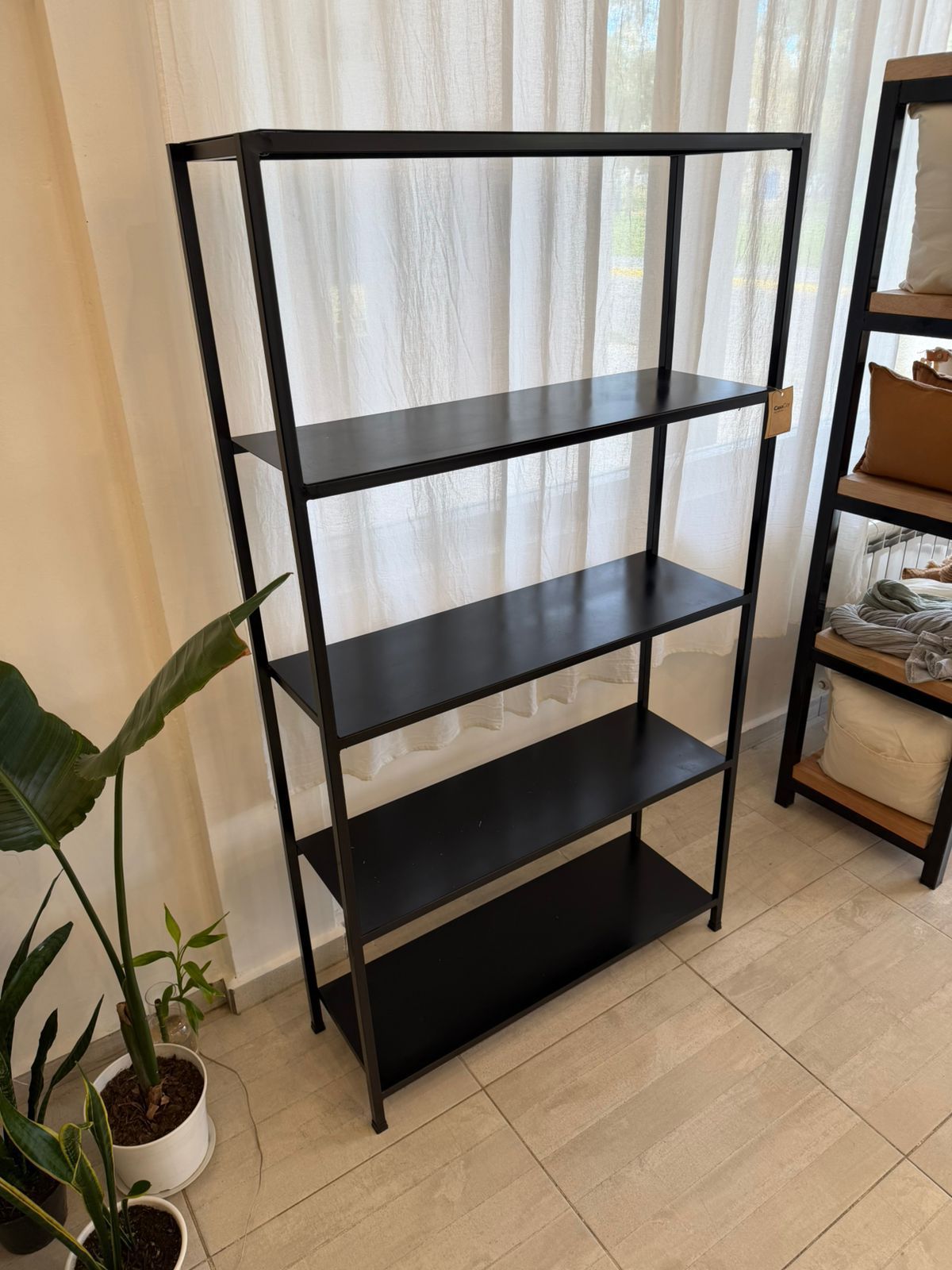 Estantería de metal negro con plantas en macetas, jabón y toallas en una habitación luminosa.