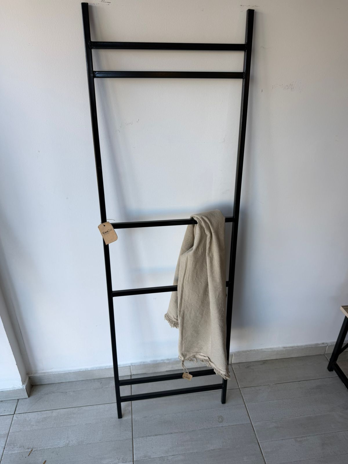 Un estante de metal negro para escaleras apoyado contra la pared, con una toalla beige extendida sobre un peldaño.