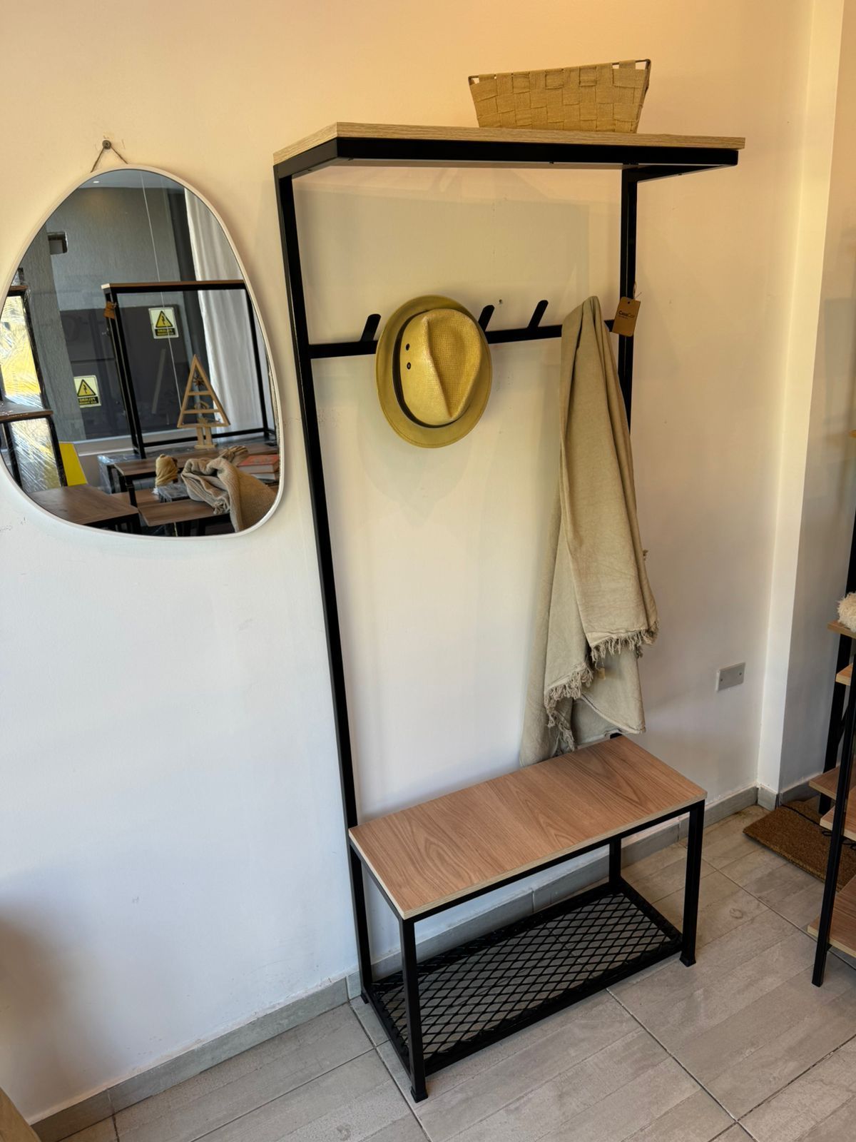 Entrada minimalista con perchero negro, banco y silla de madera sobre una alfombra tejida contra una pared blanca.