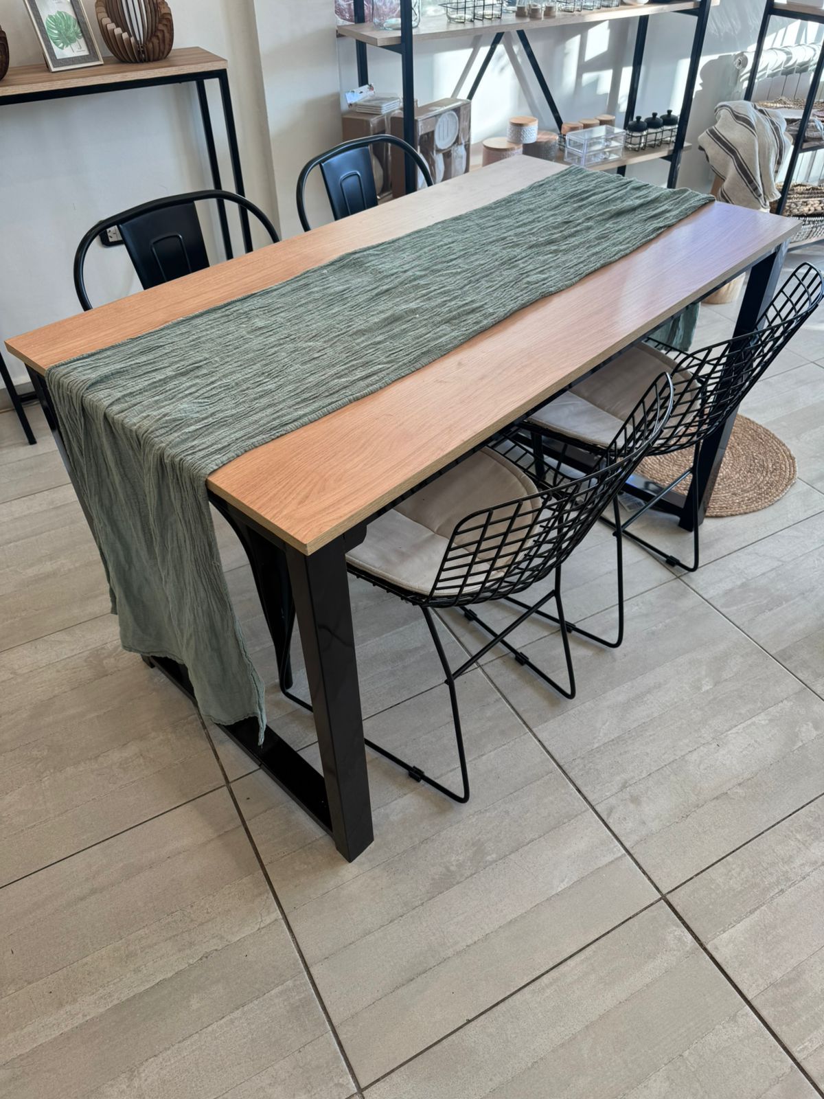 Mesa de comedor con camino de mesa tejido y sillas de alambre negro sobre un suelo de baldosas.
