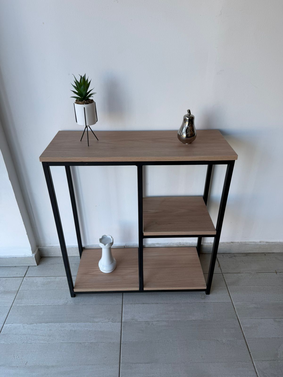 Tapiz de macramé sobre una pequeña mesa consola de madera y negra con elementos decorativos en una habitación minimalista.
