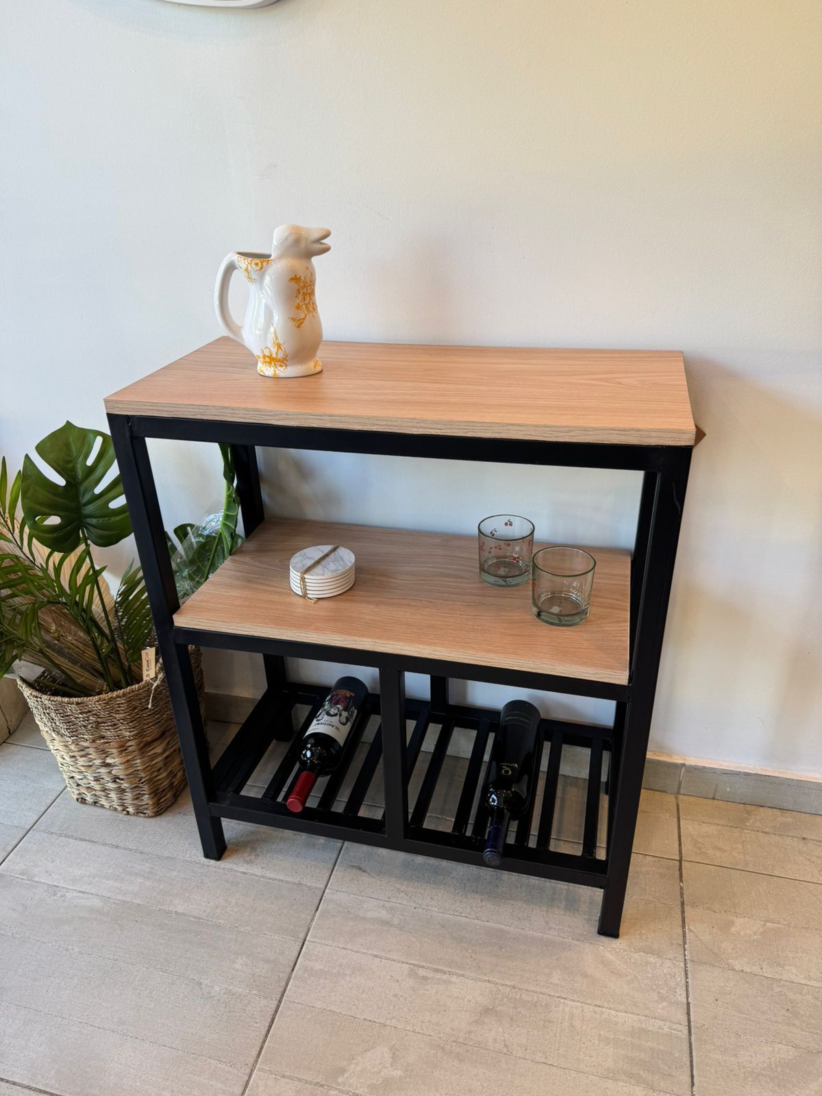 Estantería de madera y metal negro contra la pared, con una tetera, un vaso y libros en sus estantes.