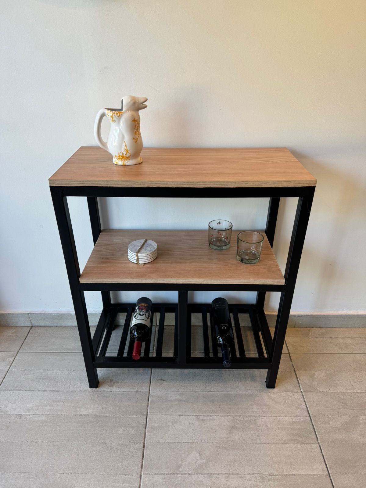 Estantería de madera y metal negro contra la pared, con una tetera, un vaso y libros en sus estantes.