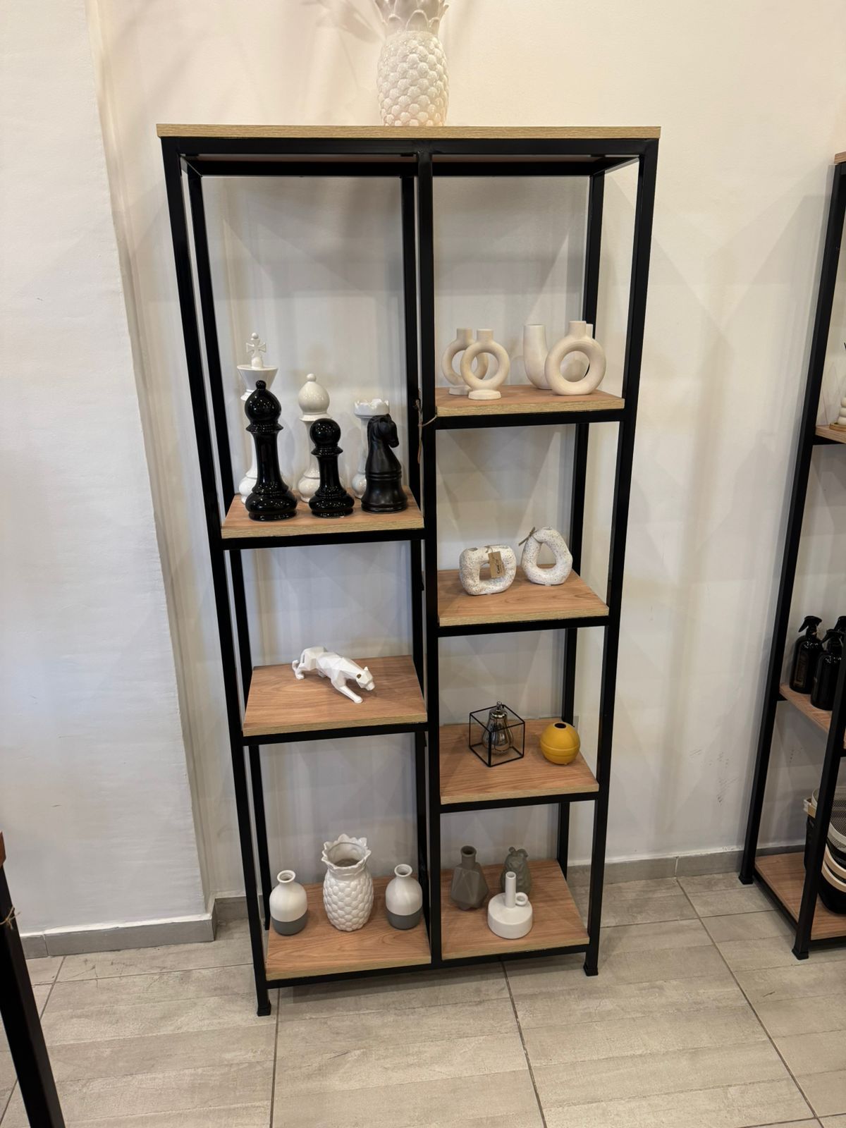 Estanterías de metal negro con pequeños jarrones decorativos y adornos sobre un suelo de baldosas.
