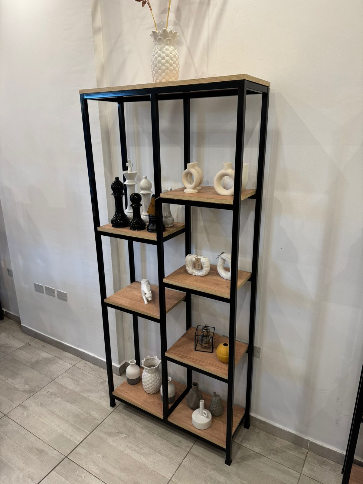 Estanterías de metal negro con pequeños jarrones decorativos y adornos sobre un suelo de baldosas.