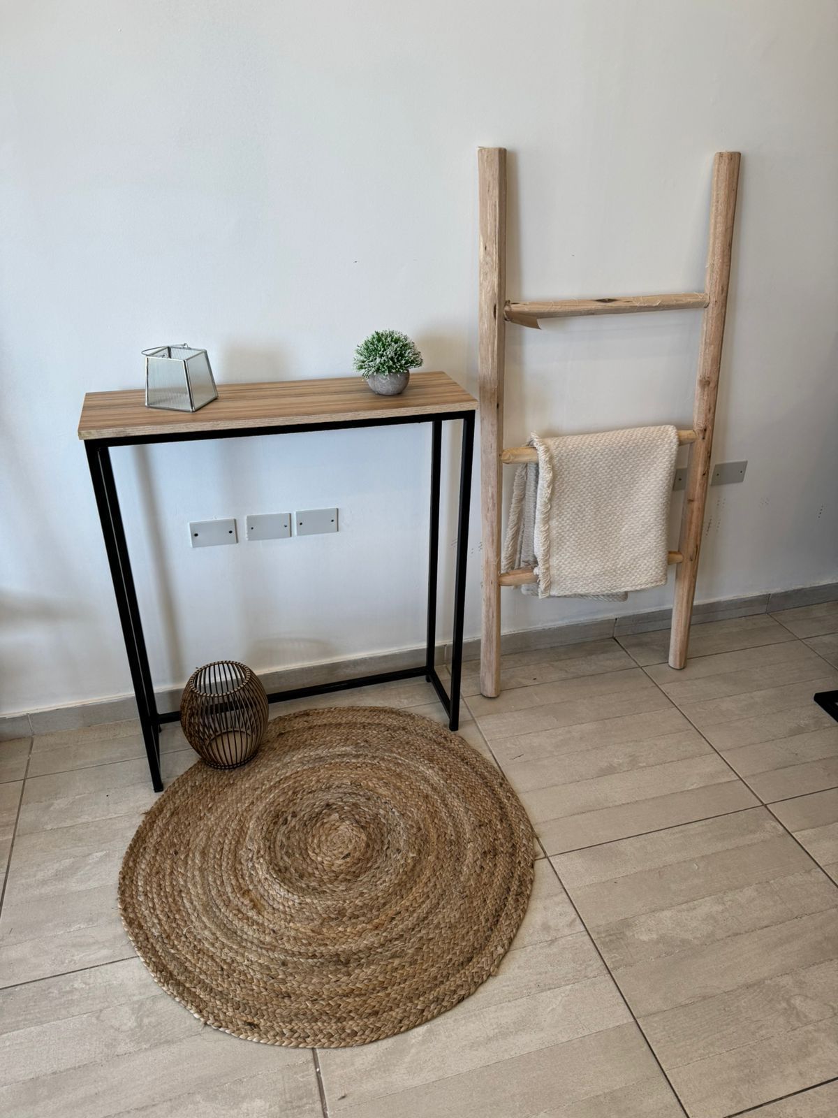 Habitación minimalista con estantería de escalera de madera, mesa pequeña, alfombra tejida.