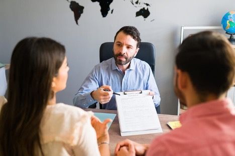 a couple on one end of a table, a man on the other holding up a document on a clipboard