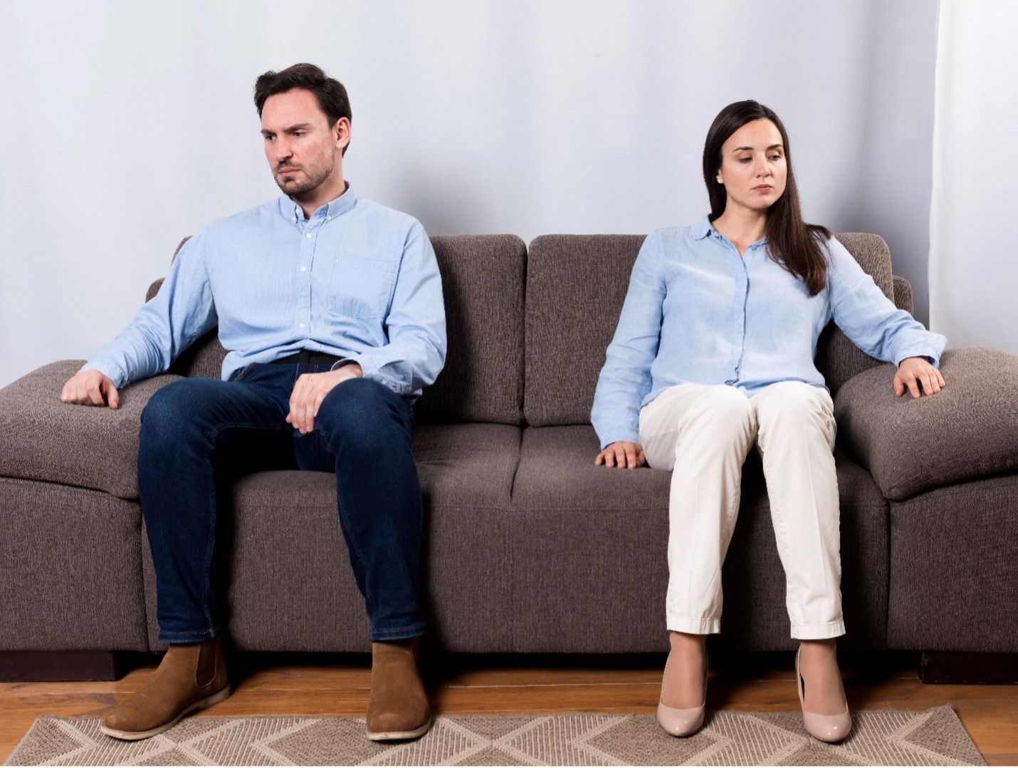 Two people sitting apart on a gray couch, looking away with serious expressions.