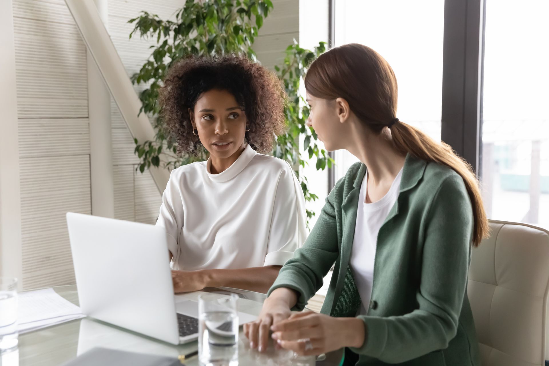Two women are sitting at a table looking at a laptop computer.