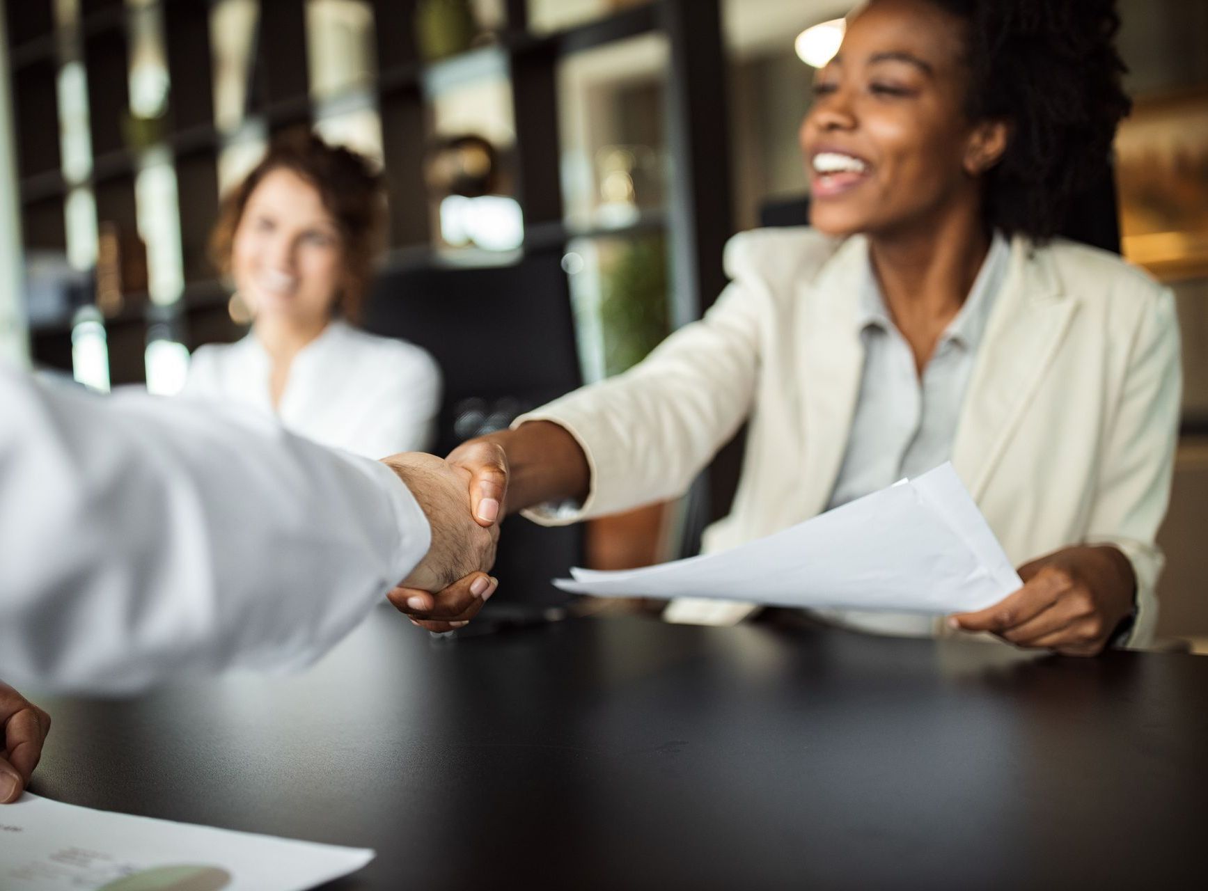 A woman is shaking hands with a man while holding a piece of paper.