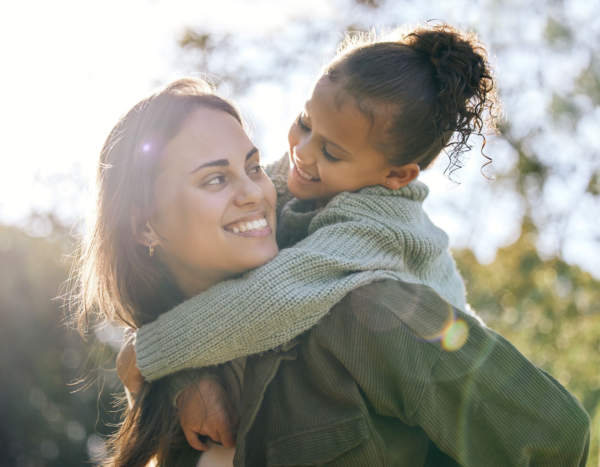 A woman is carrying a little girl on her back in a park.