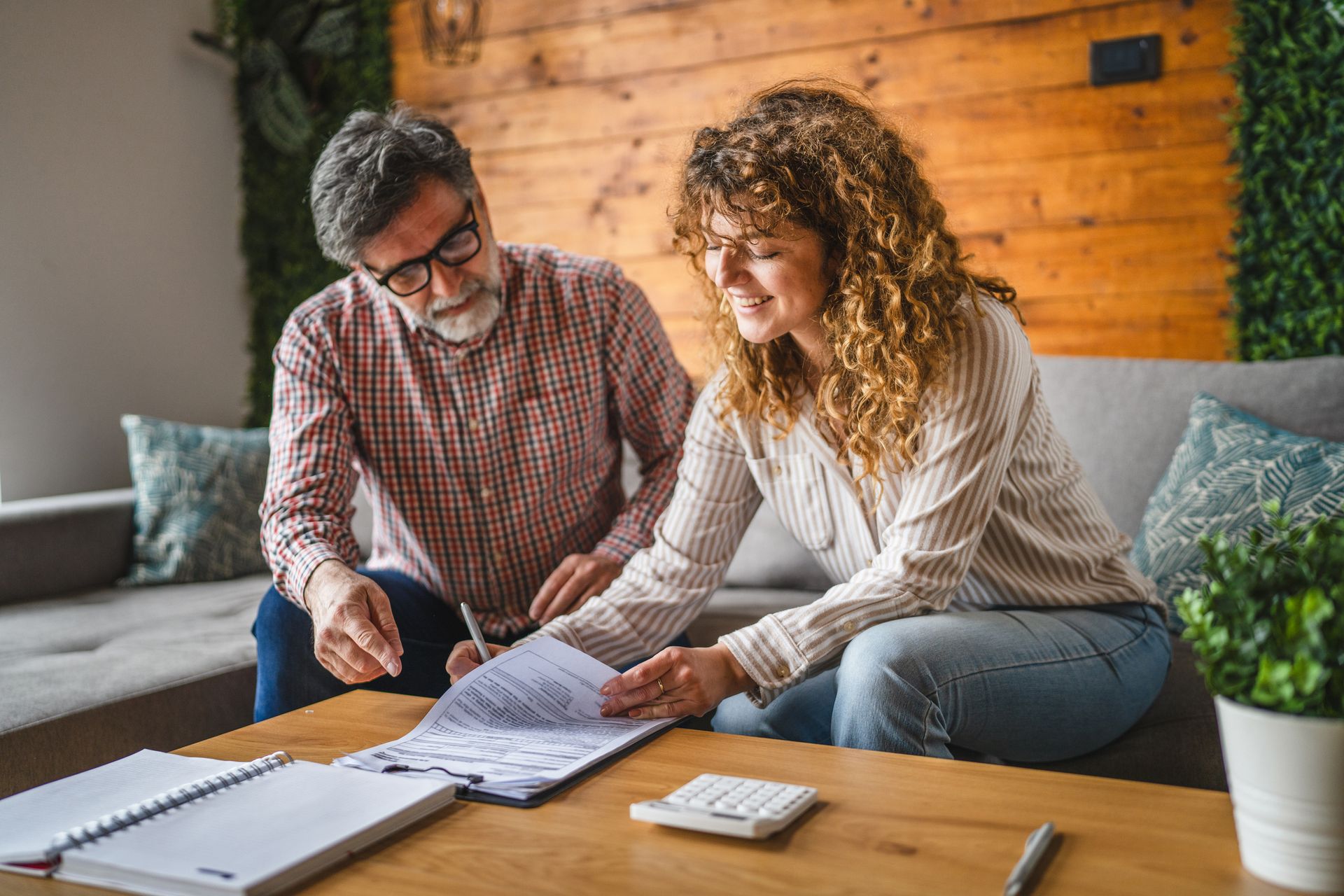 a man and woman sit on a couch signing documents