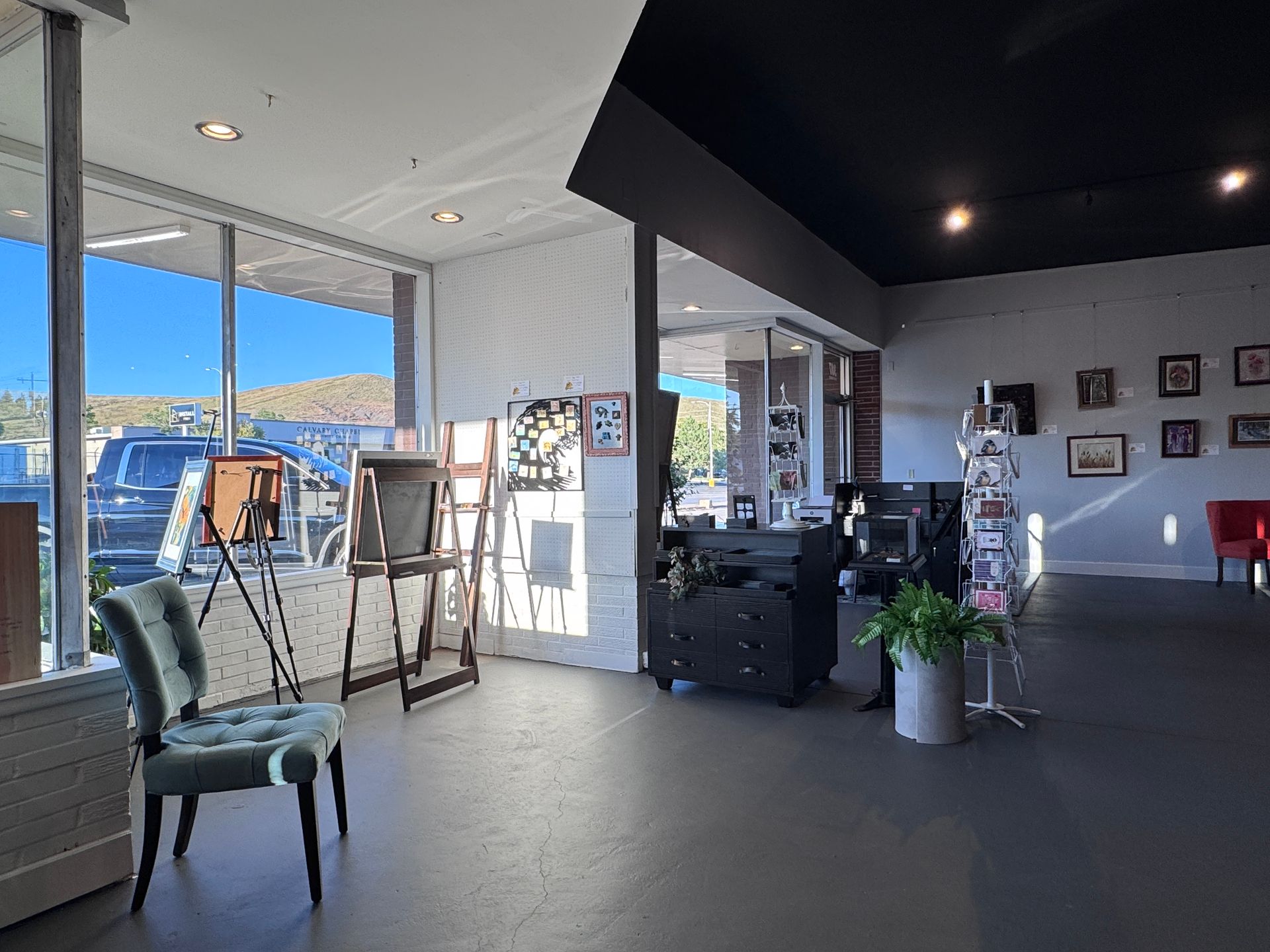 Interior shot of a business with furniture, artwork, and large windows looking outside to a sunny day.