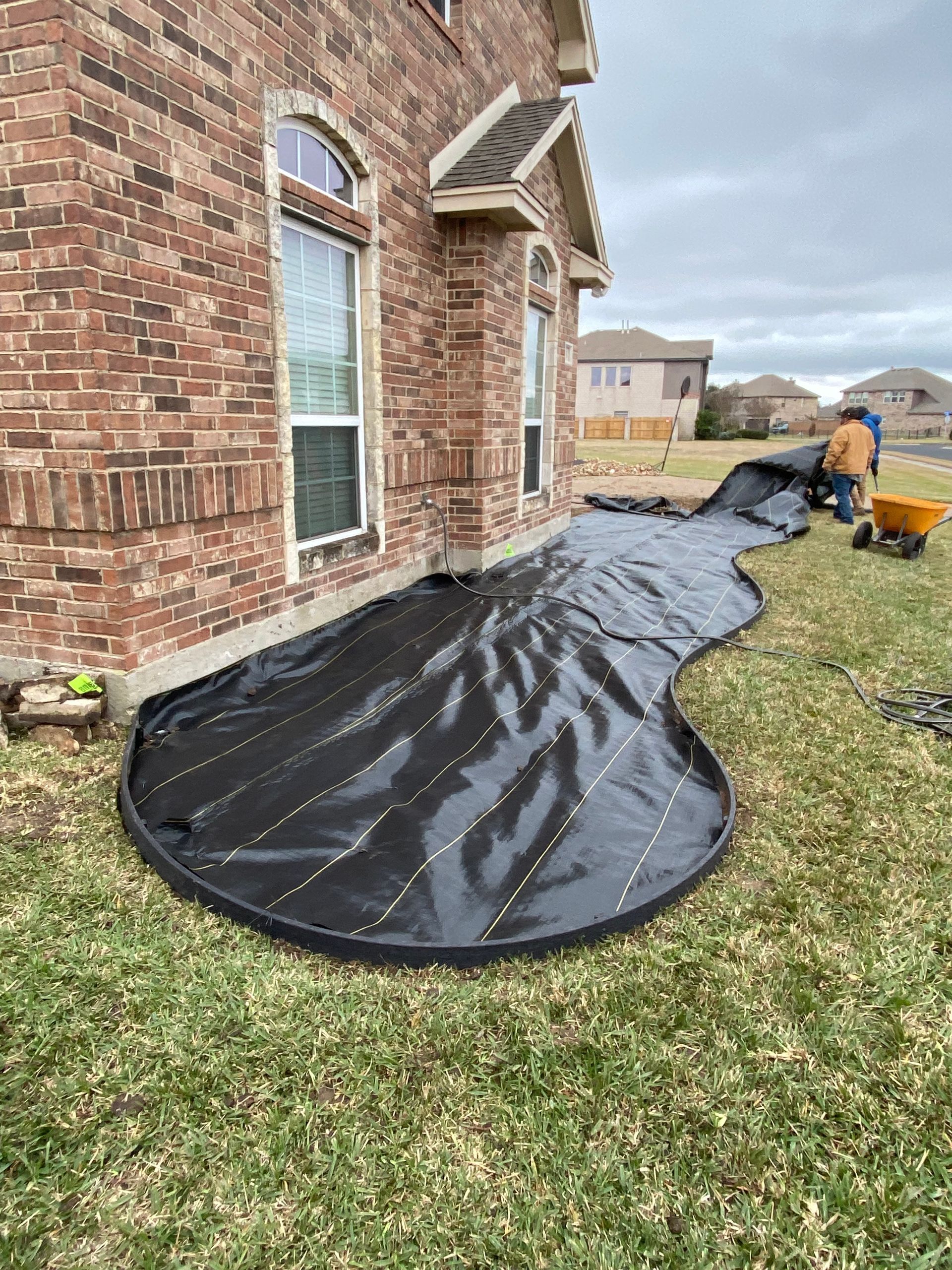 A brick house with a black tarp on the ground in front of it.