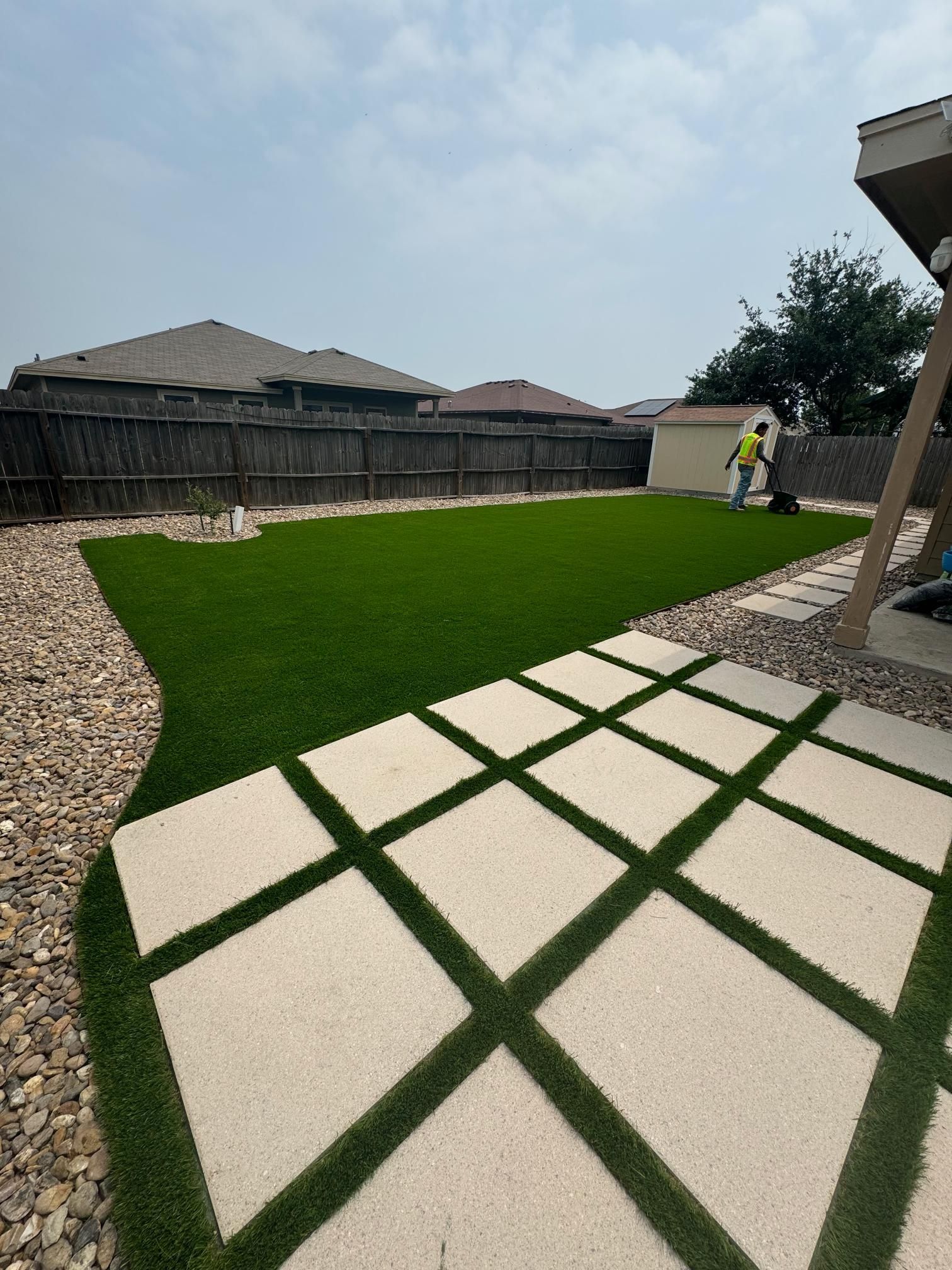 A lawn with a walkway and a fence in the background.