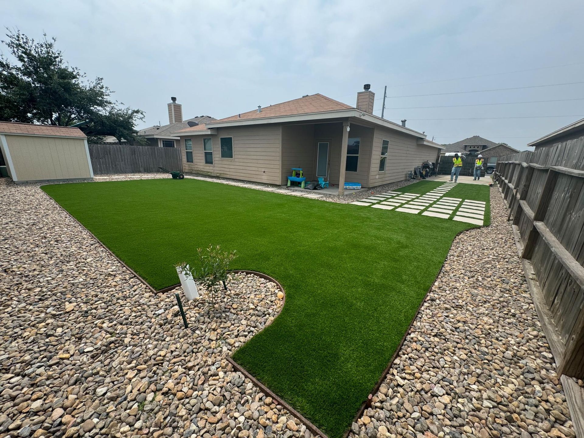 A backyard with a lot of grass and rocks and a house in the background.