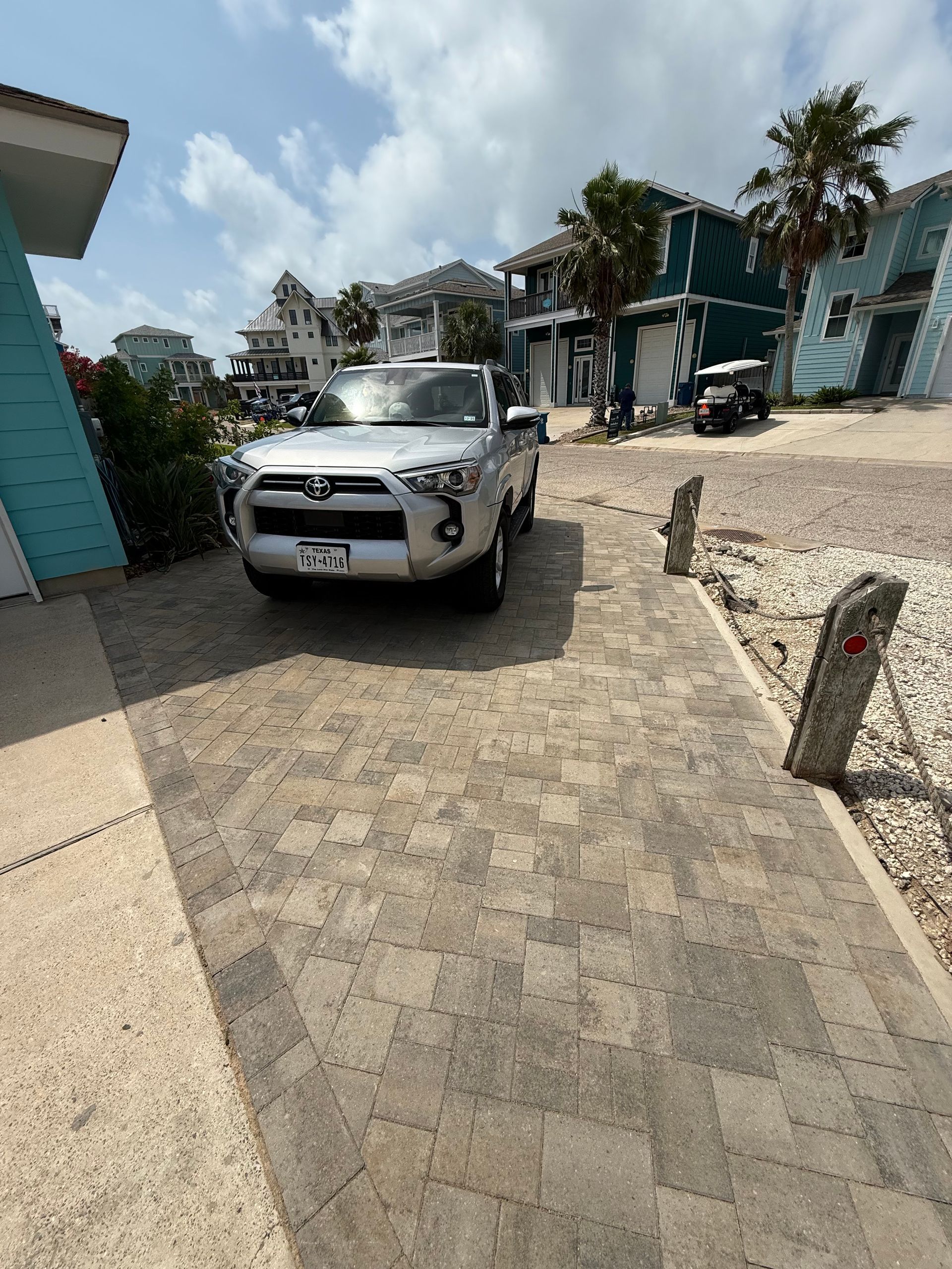 A silver SUV parked on a paved driveway in front of beach-style houses under a bright, sunny sky.