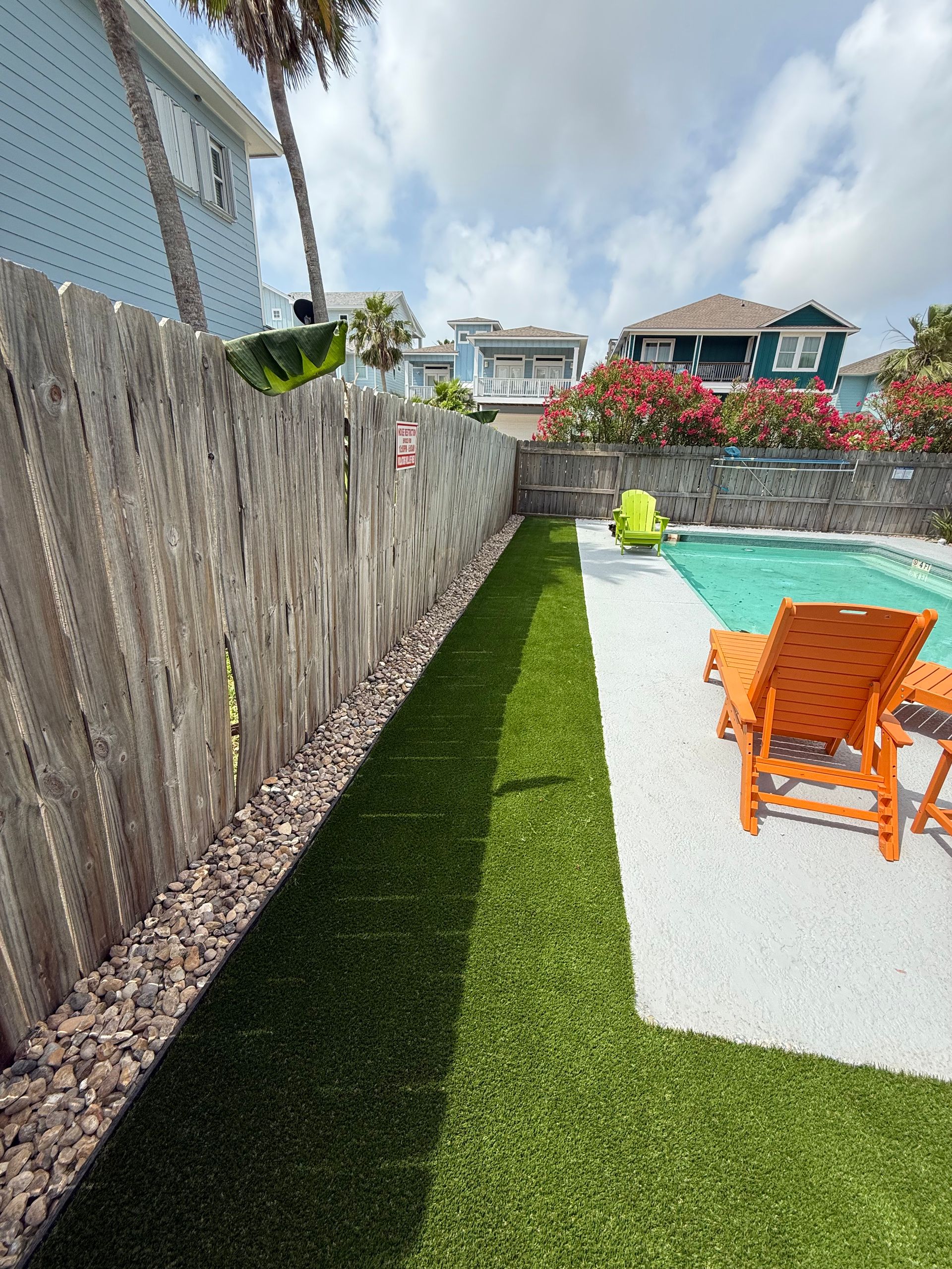 An orange lounge chair sits beside a backyard pool next to a wooden fence and artificial grass strip.