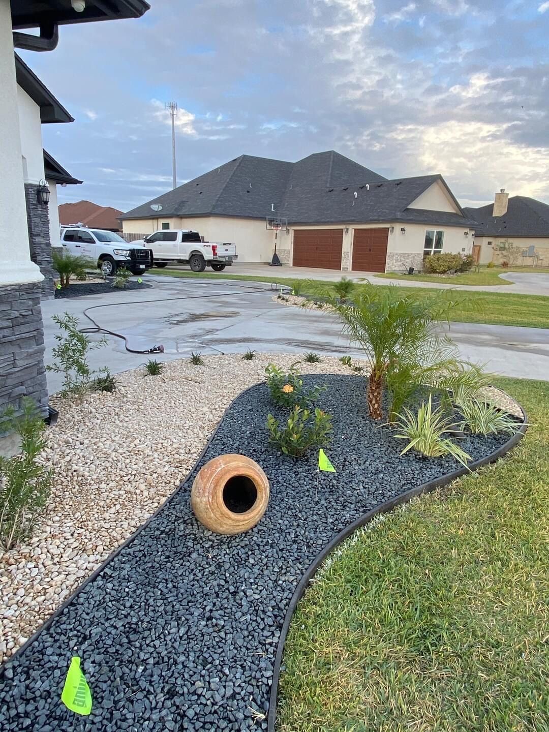 A large vase is sitting on the side of a gravel path in front of a house.