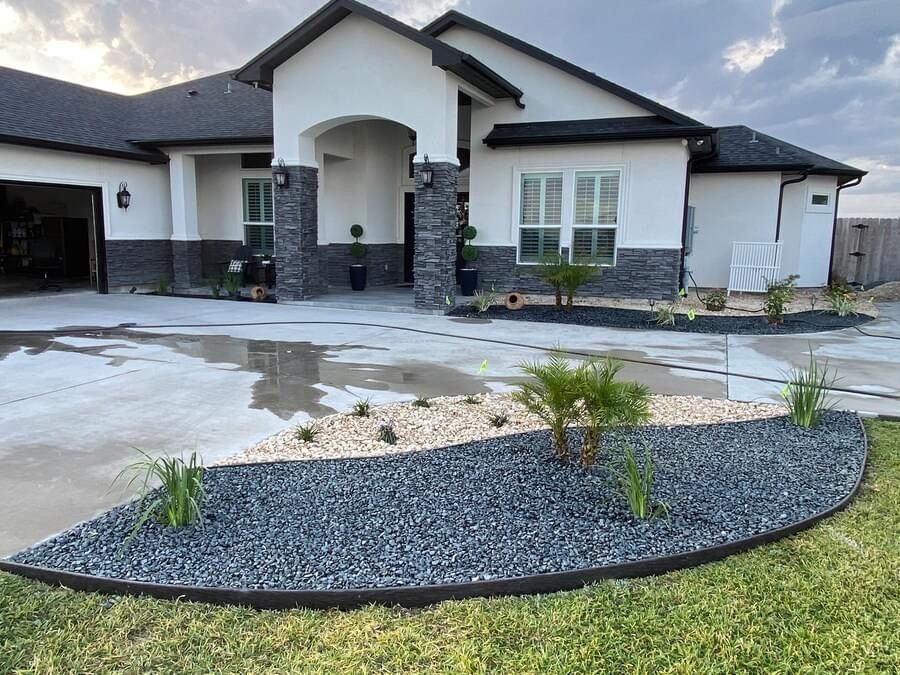 A white house with a black roof and a garden in front of it.