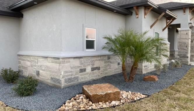 A house with a palm tree and rocks in front of it.
