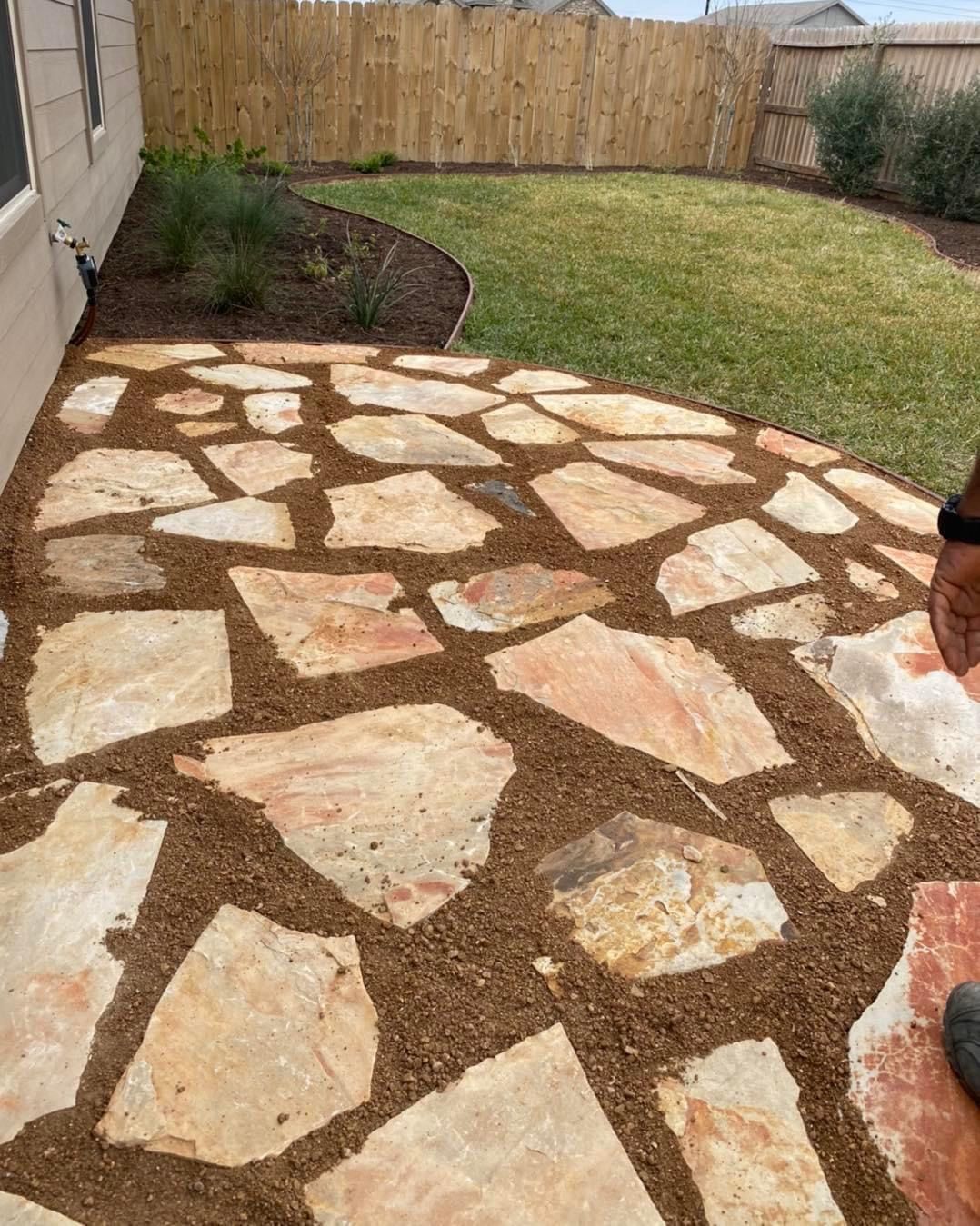 A person is standing on a stone walkway in a backyard.