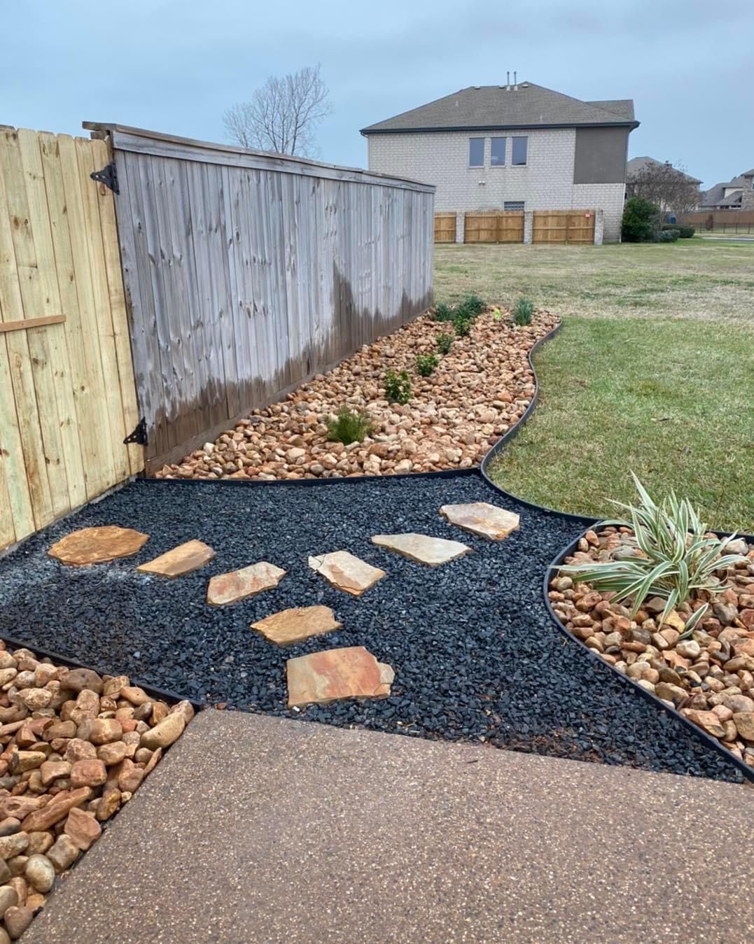 A backyard with a wooden fence and a walkway surrounded by rocks and gravel.