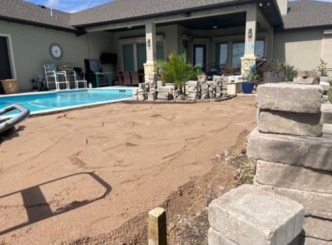 A stack of bricks is sitting in front of a house next to a pool.