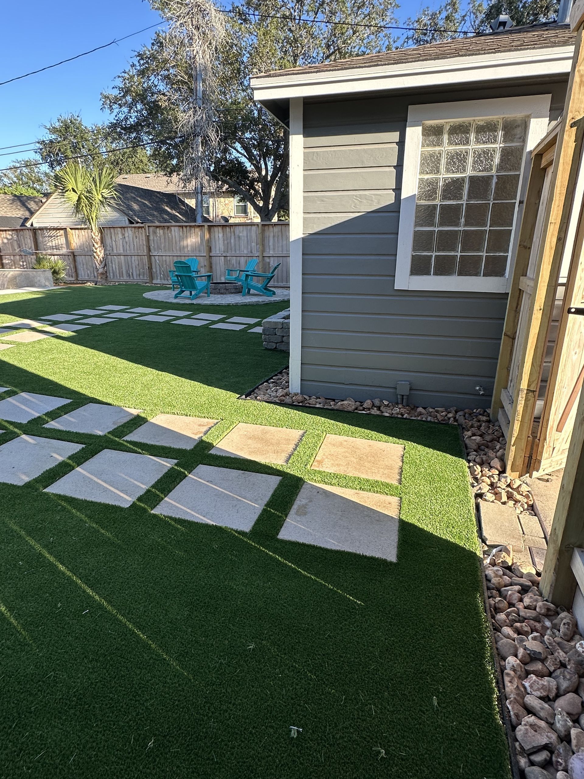 A backyard with artificial grass, stone pavers, a grey shed, and two teal outdoor chairs in the background.