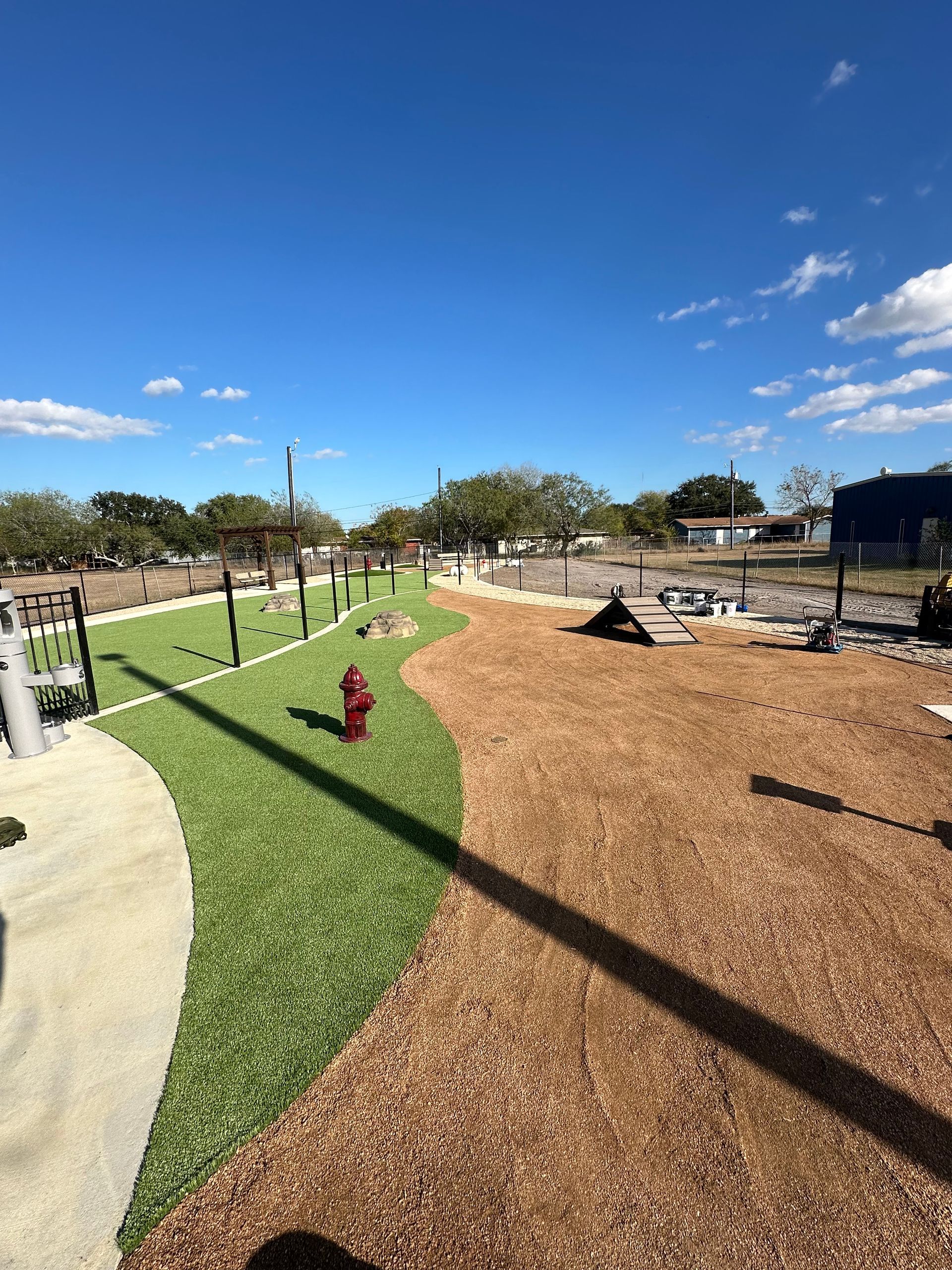 Park landscape with green lawn, wood-chip paths, fire hydrant, and blue sky with clouds