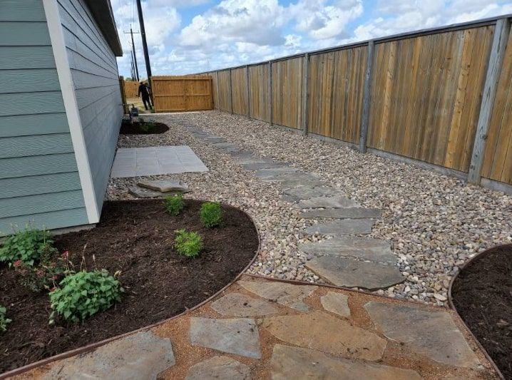 A stone walkway leading to a house with a wooden fence in the background.