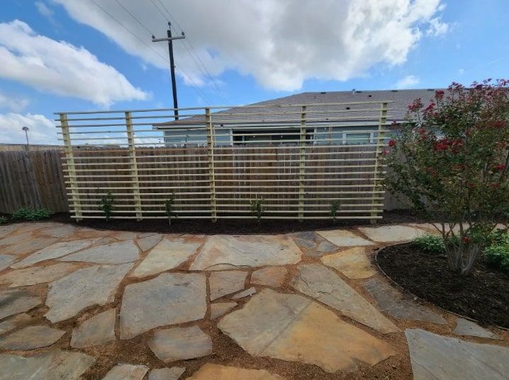A stone patio with a wooden fence and a house in the background