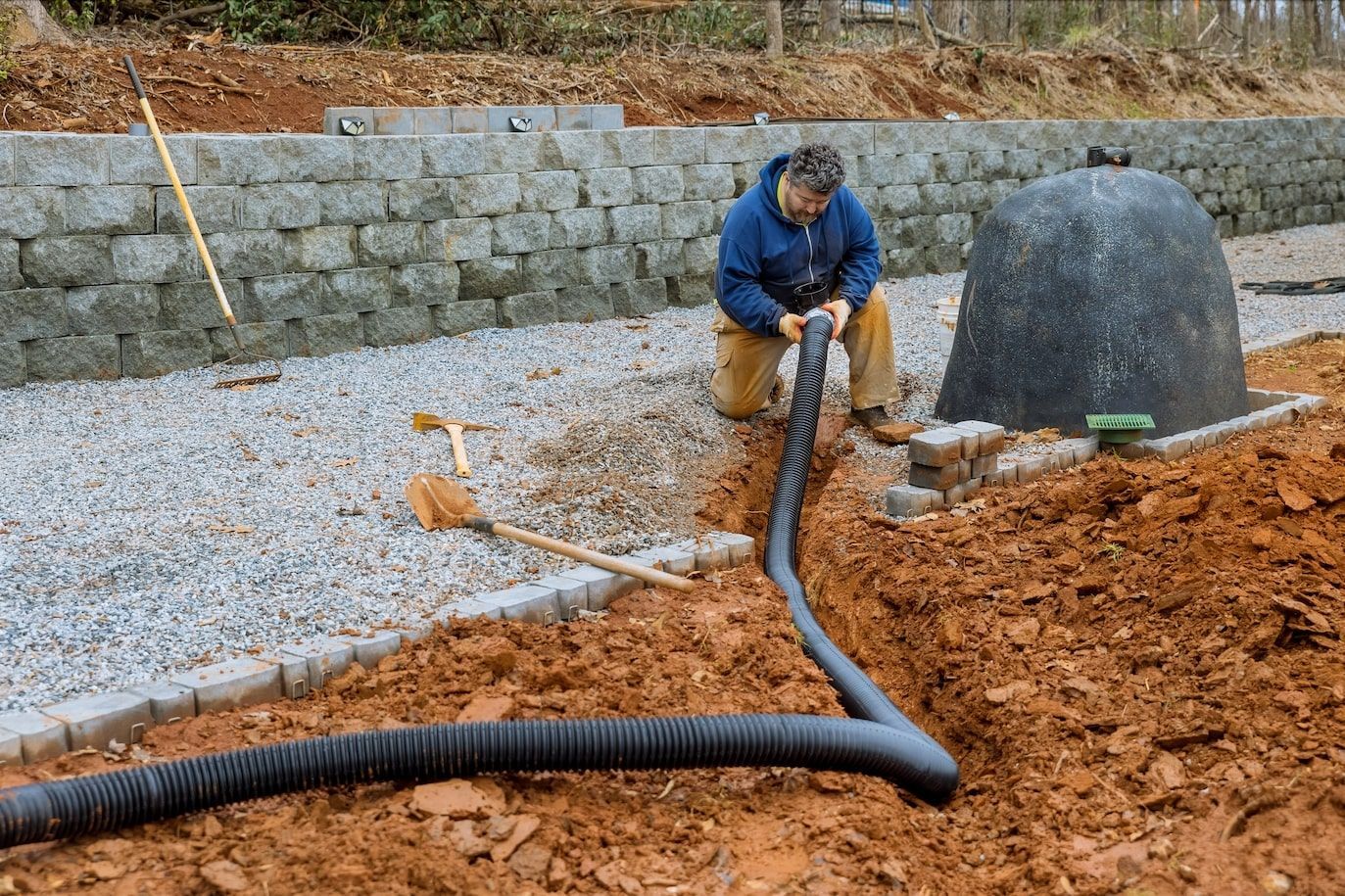 A man is kneeling down in the dirt next to a hose.