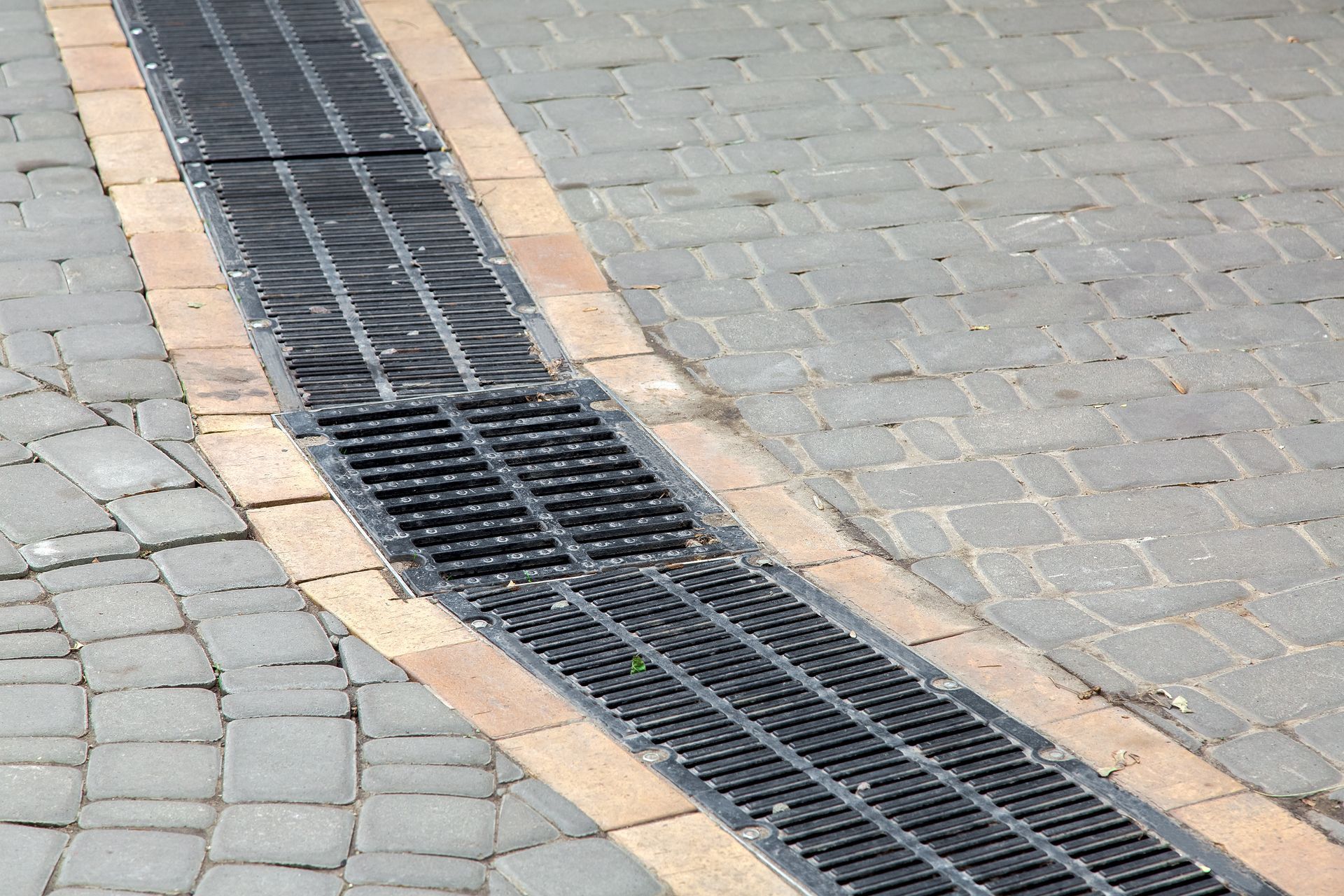 Curved black drainage grate set into gray cobblestones with tan border stones