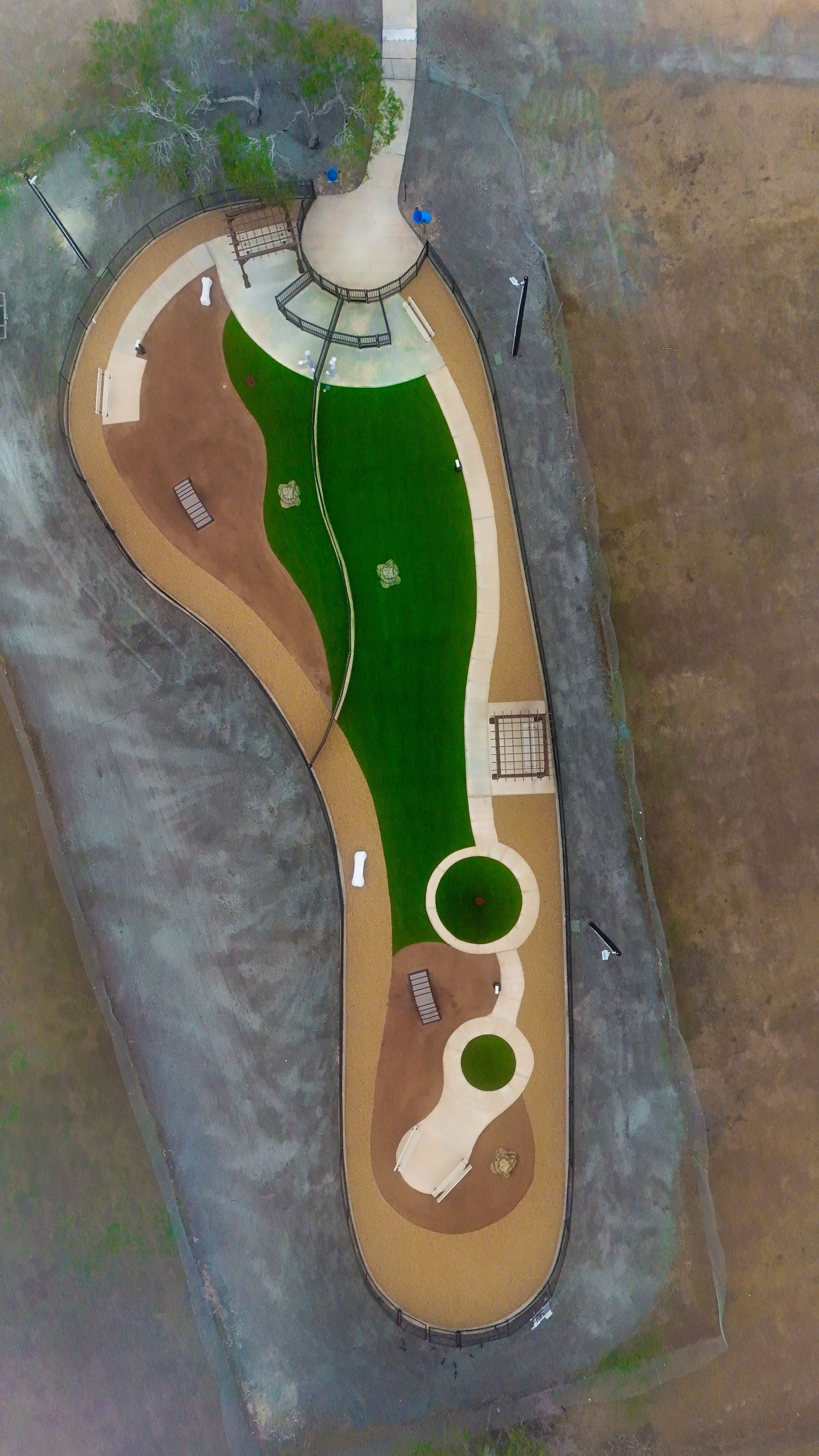 Aerial view of a foot-shaped park featuring paths, green turf, tan mulch areas, and small seating or play structures.