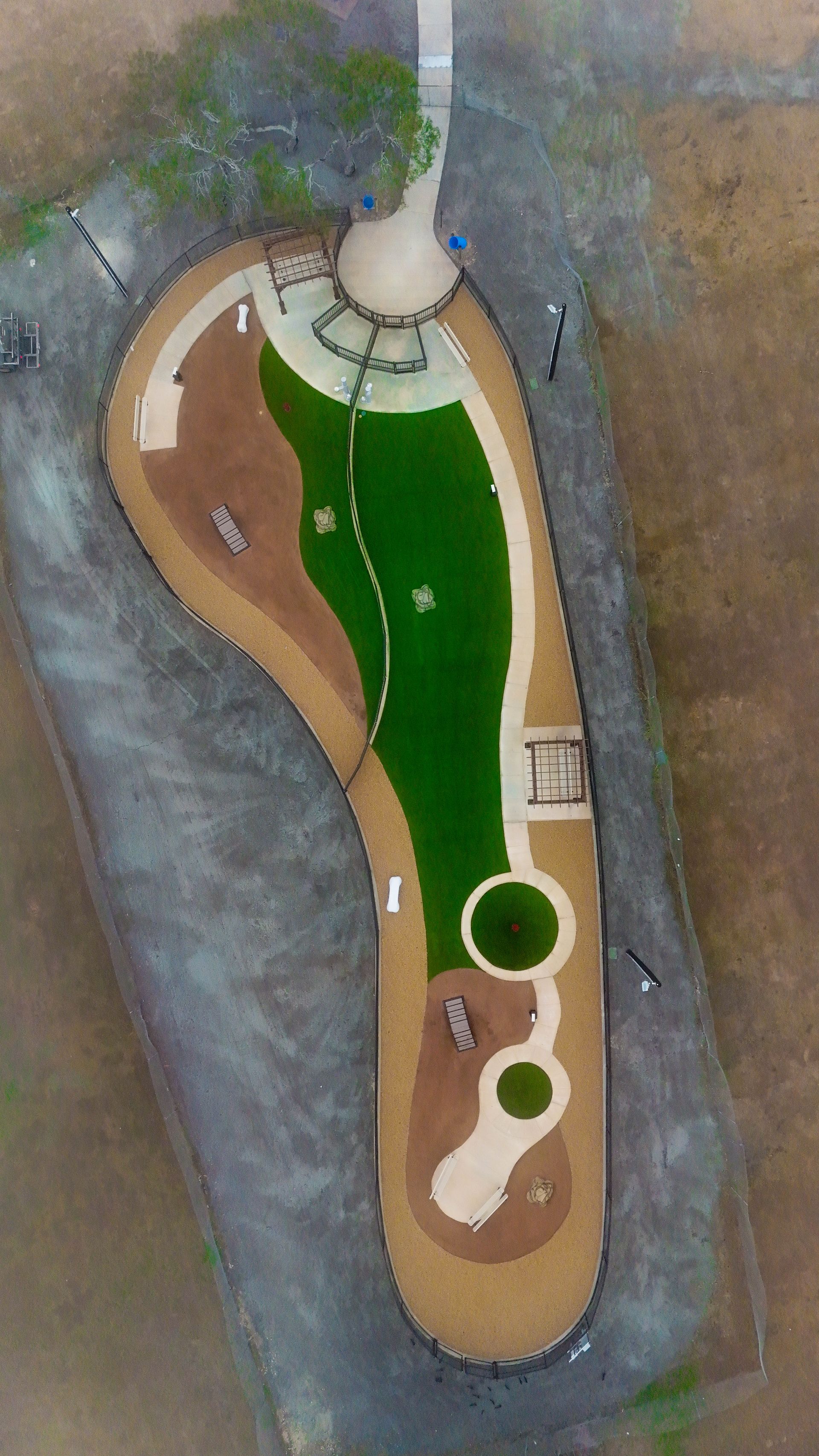 Aerial view of a long, foot-shaped park featuring walking paths, green turf areas, and playground equipment.