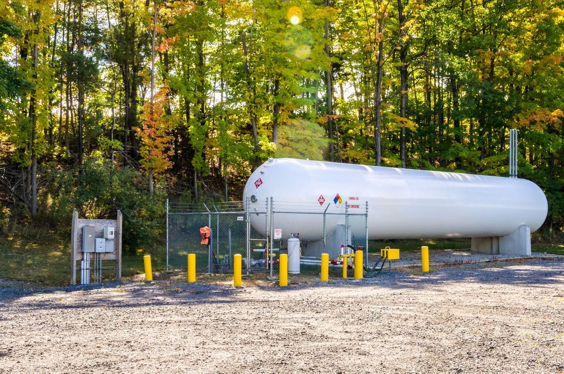 View of a white bulk propane tank on a sunny autumn day View of a white bulk propane tank on a sunny autumn day