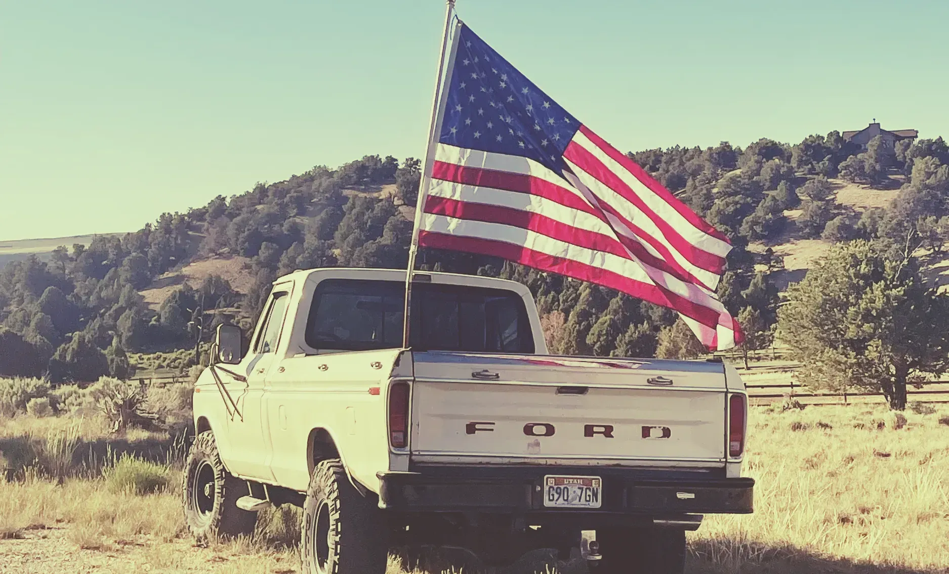 A white ford truck with an american flag in the back