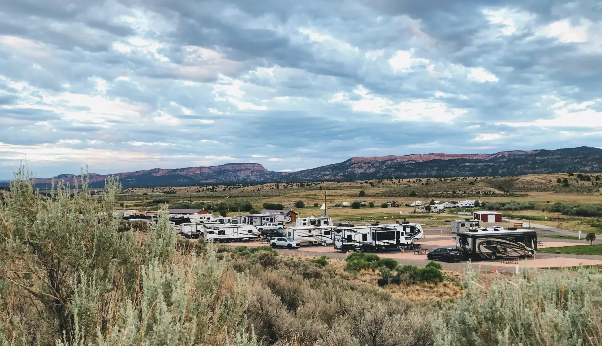 A group of rvs are parked in a field with mountains in the background.