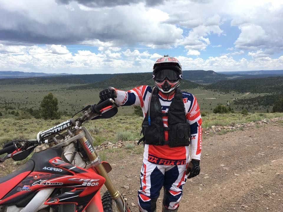 A man is standing next to a dirt bike on a dirt road.