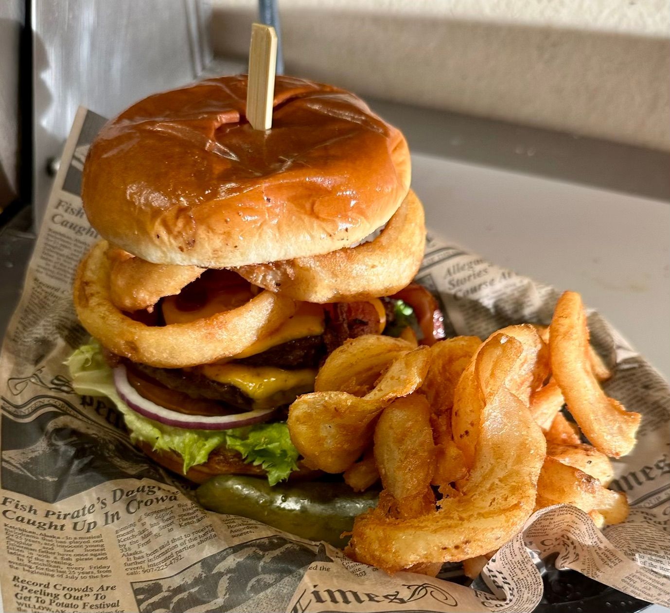A hamburger with onion rings and french fries on a newspaper