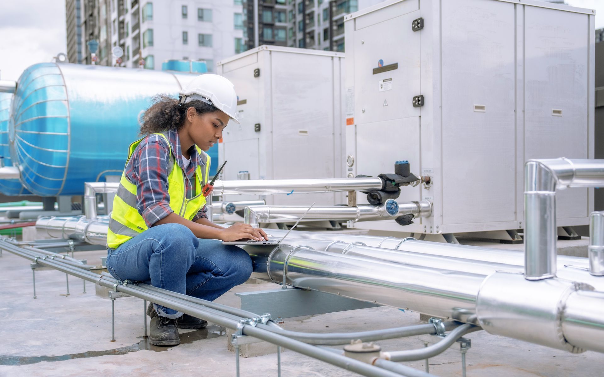 A woman is kneeling down on a roof looking at a laptop.