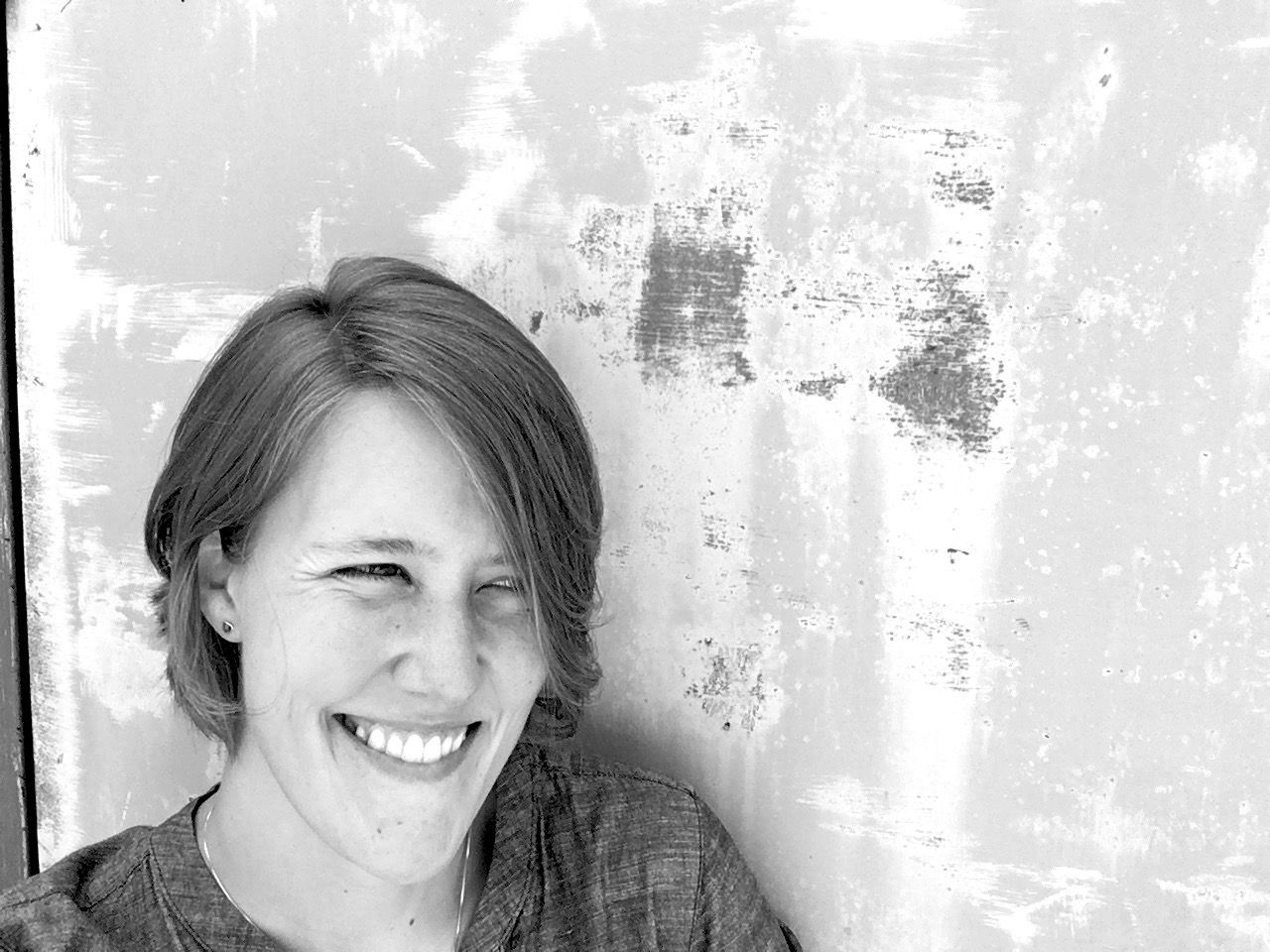 A woman is smiling in front of a wall in a black and white photo.